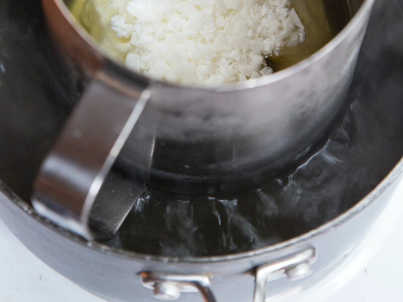 White wax that is starting to melt in a metal jug over some heat.